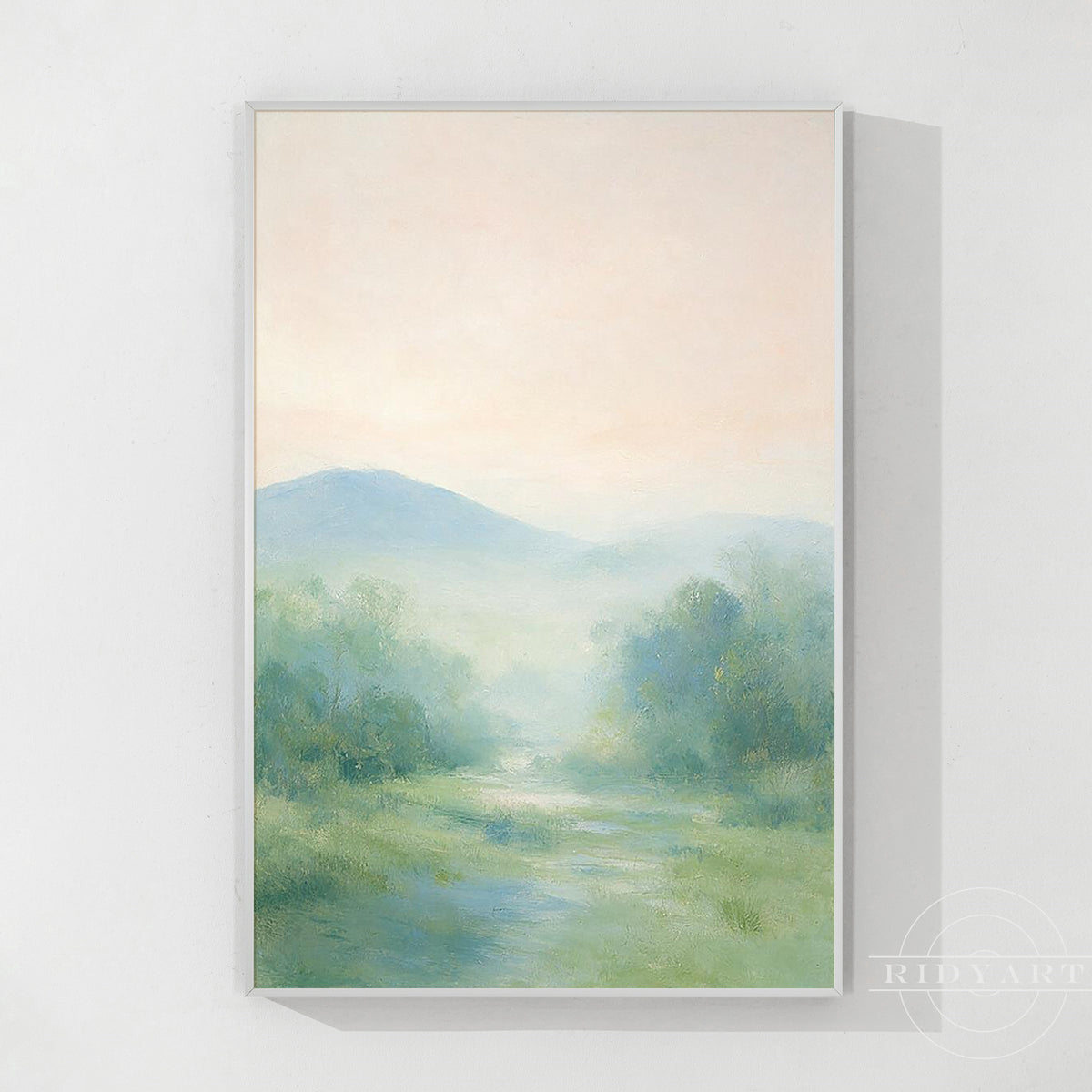 Original misty valley landscape painting in a light wood frame, with a blush pink sky, blue hills and green meadows on a white wall.