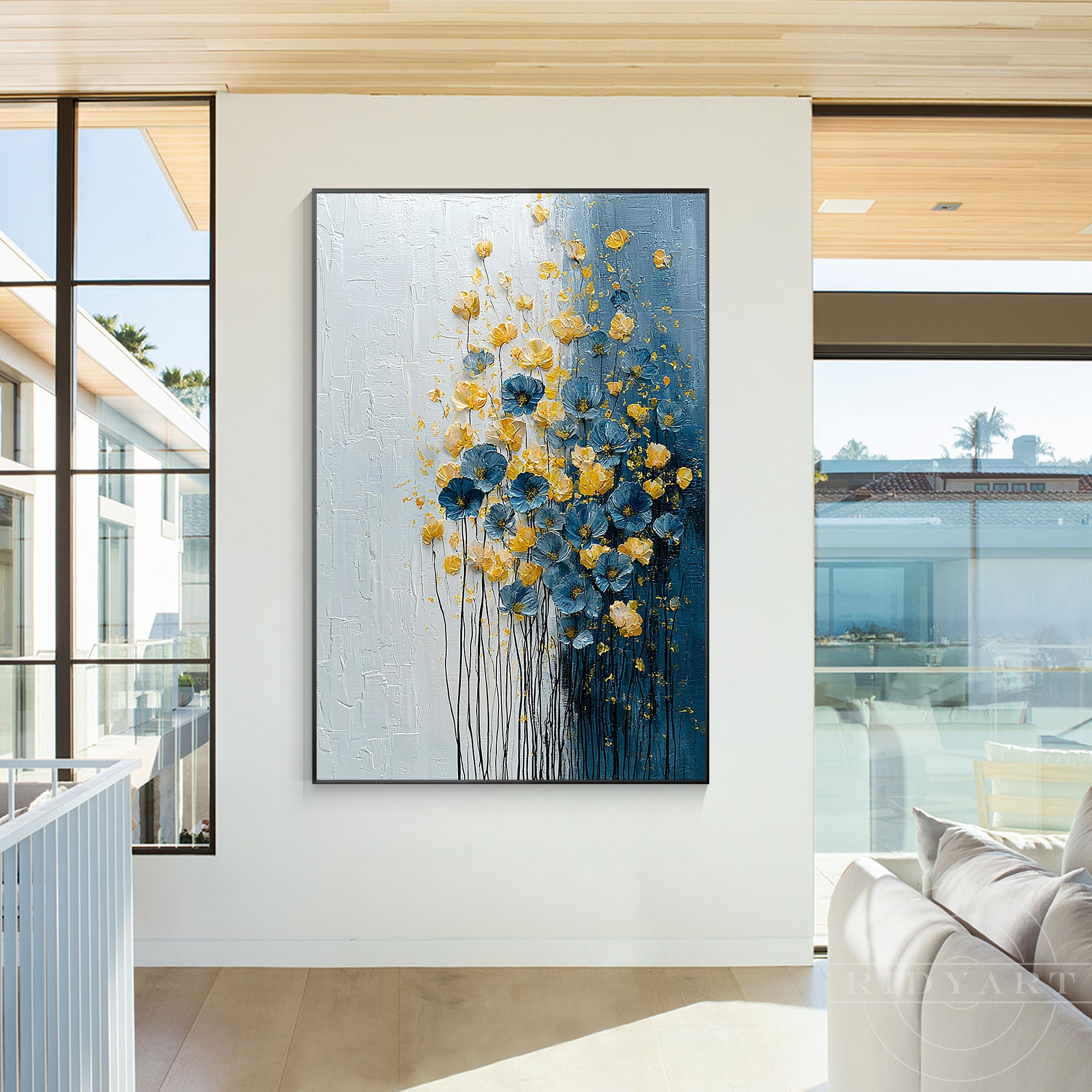 Large vertical 3D floral textured canvas art with blue and yellow flowers hanging in a bright modern living room next to large glass windows.