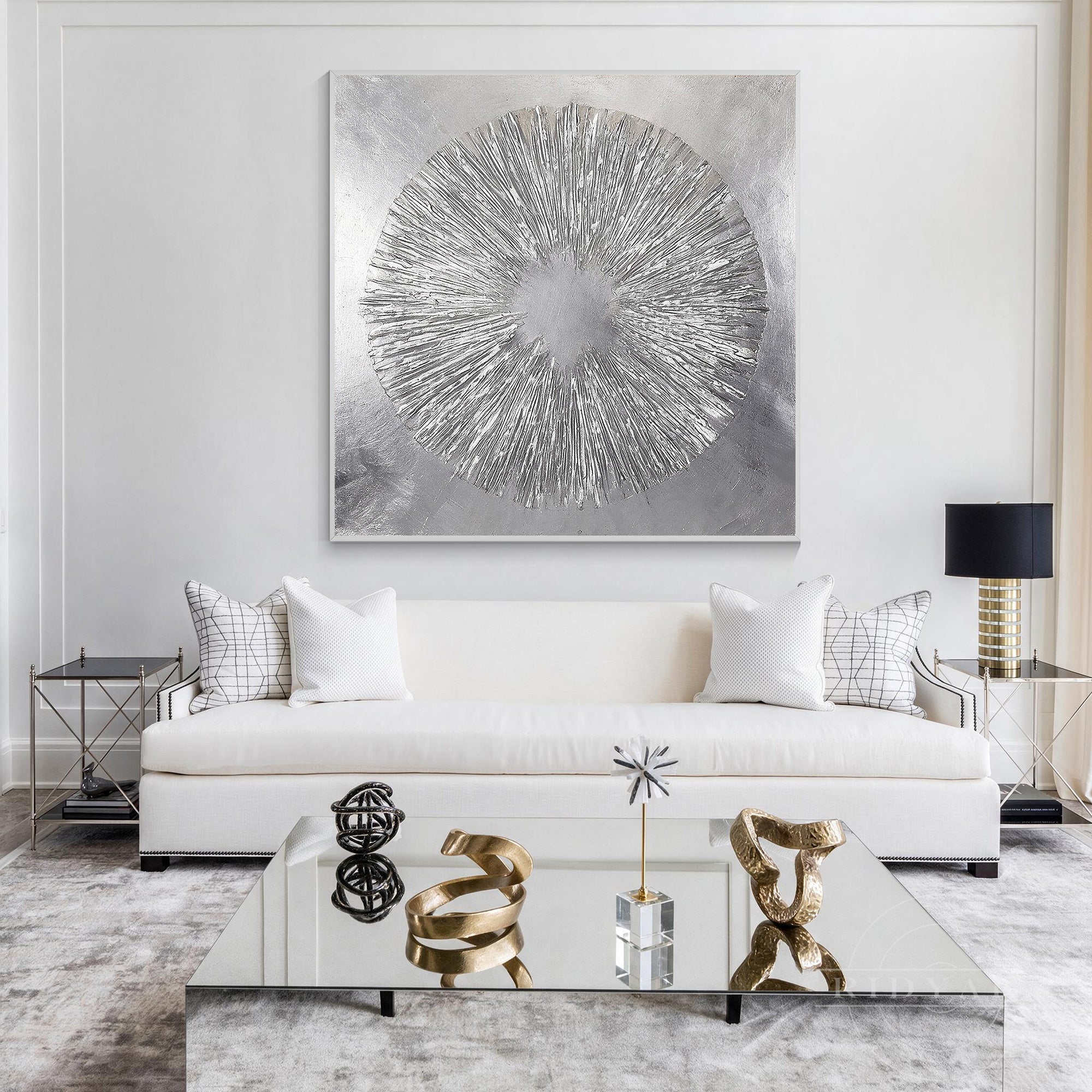 Oversized square silver leaf sunburst canvas painting mounted above a modern white sofa with decorative pillows and a glass coffee table.