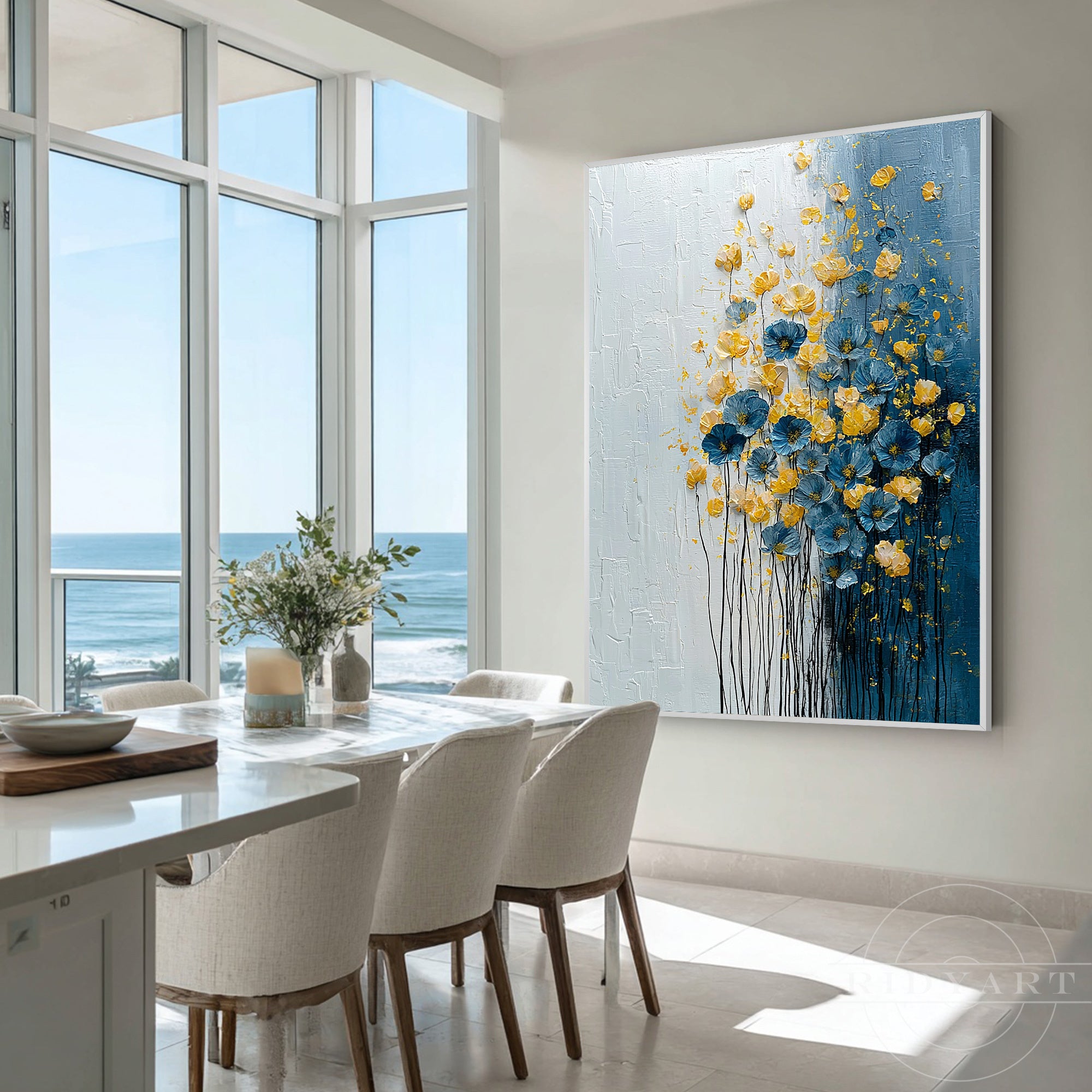 Impasto blue and yellow floral canvas wall art hanging in a bright coastal dining room overlooking the ocean.
