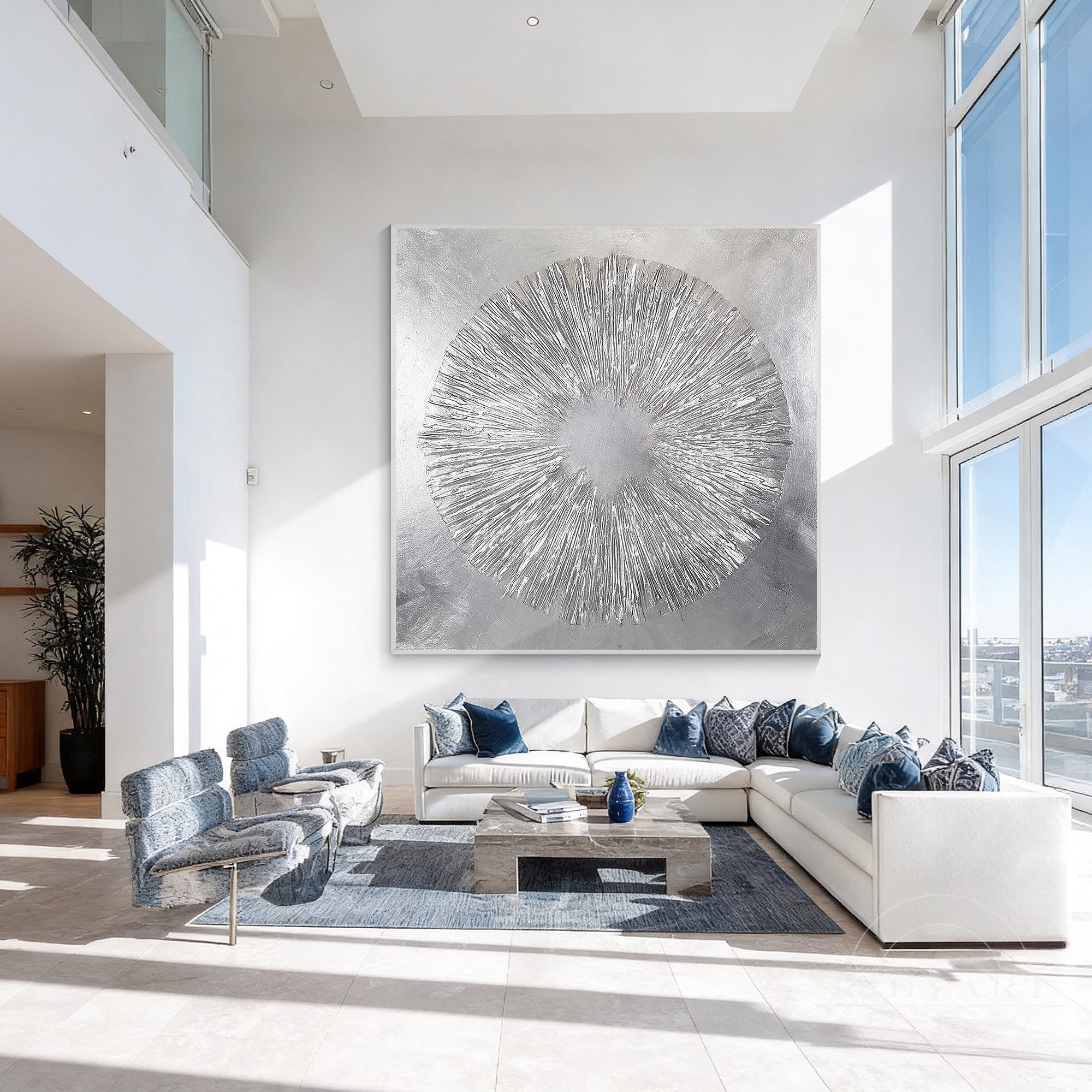 Extra large square silver sunburst canvas painting centered on a tall white wall in a high-ceiling living room with blue accent armchairs.