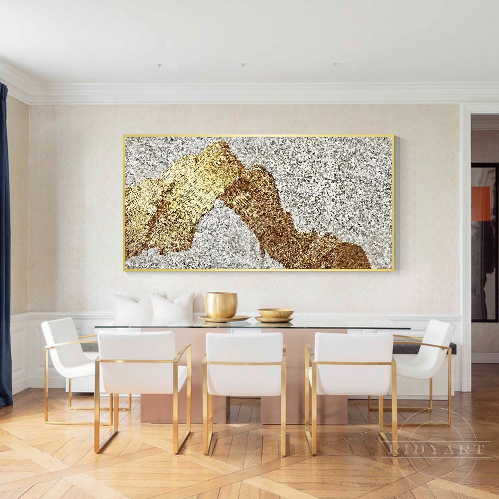 Horizontal 3D textured gold abstract canvas painting mounted in a modern luxury dining room above a glass table with white chairs.