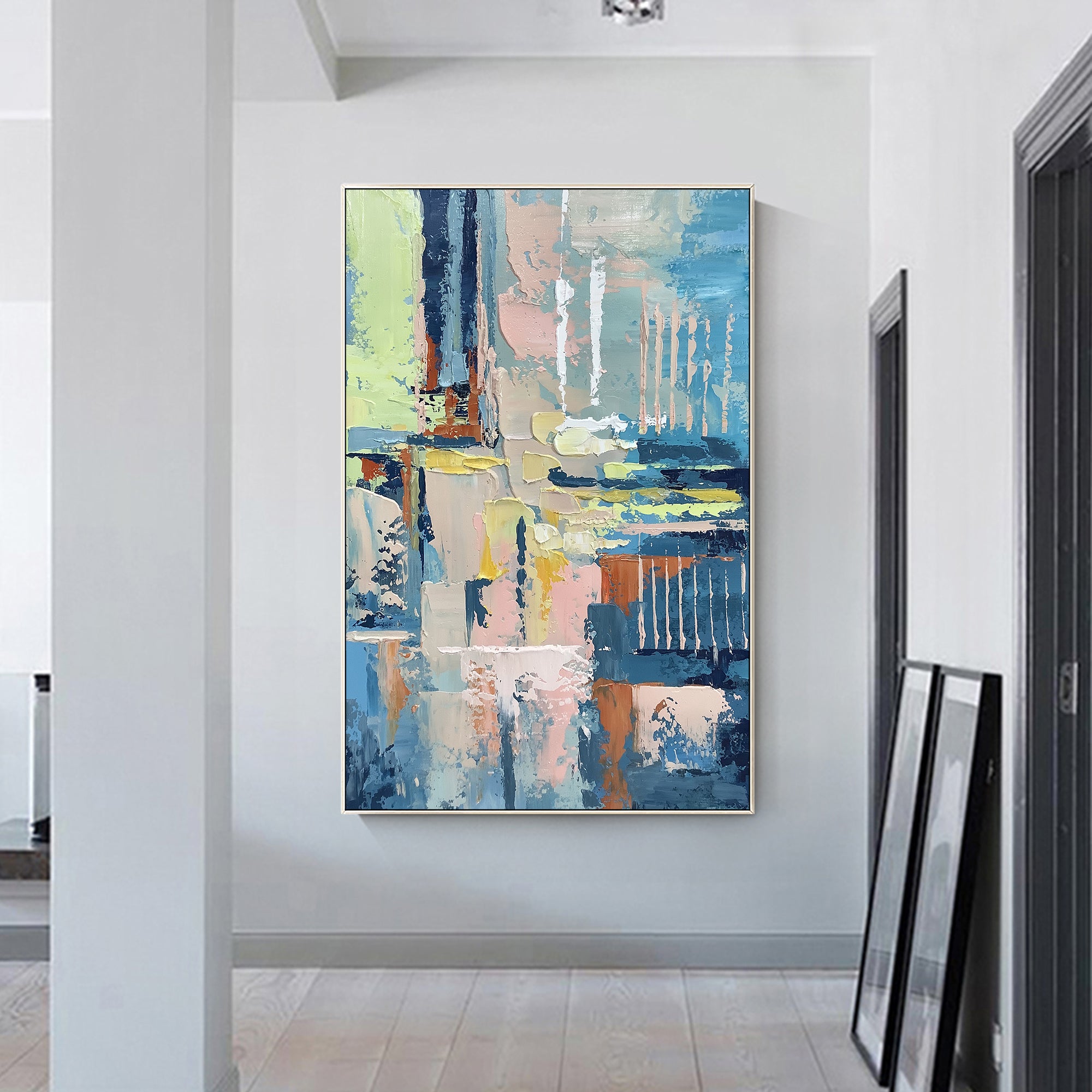 Framed abstract wall art with bold blue, soft pink, and yellow oil painting texture on a white wall background.
