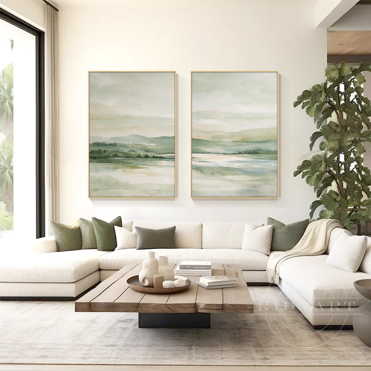 Soft green mountain landscape paintings with tranquil lake scenery and gold frames above a light-toned living room sofa.