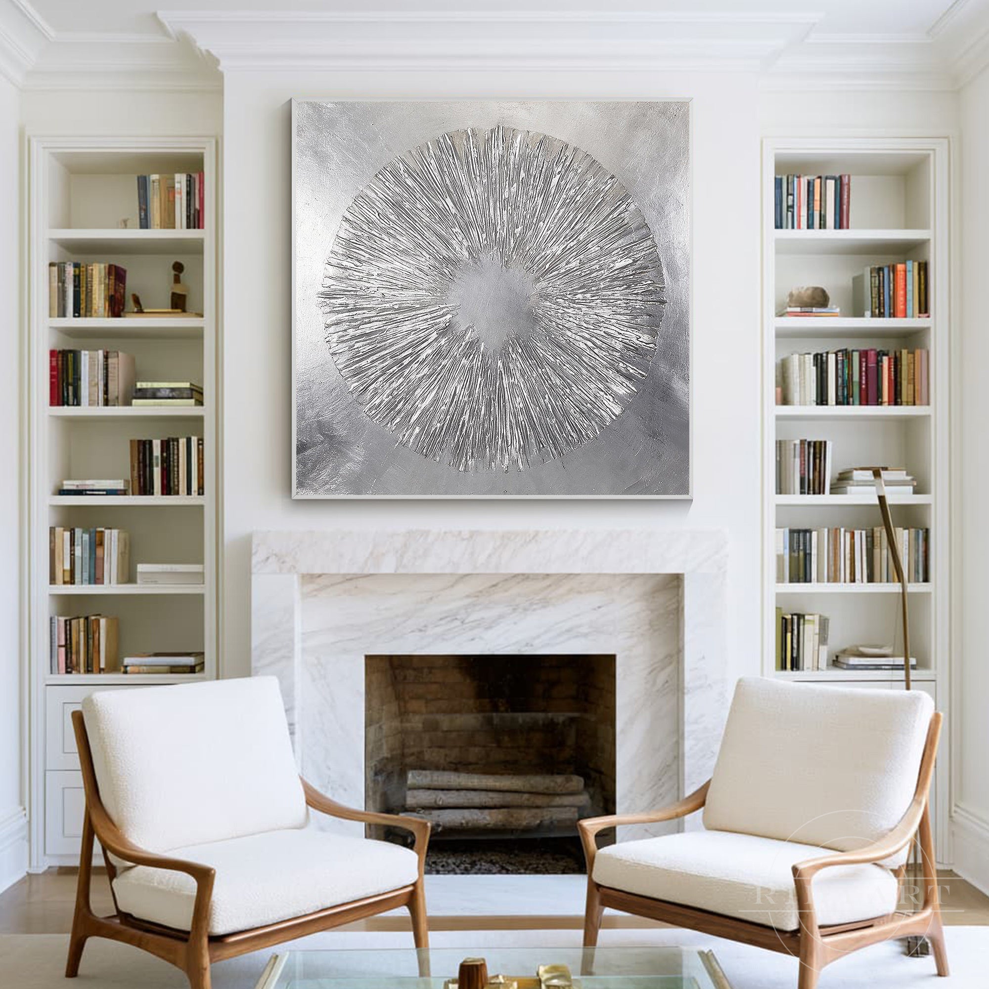 Large square textured silver foil starburst artwork framed in silver, hanging over a classic marble fireplace flanked by white built-in bookshelves.