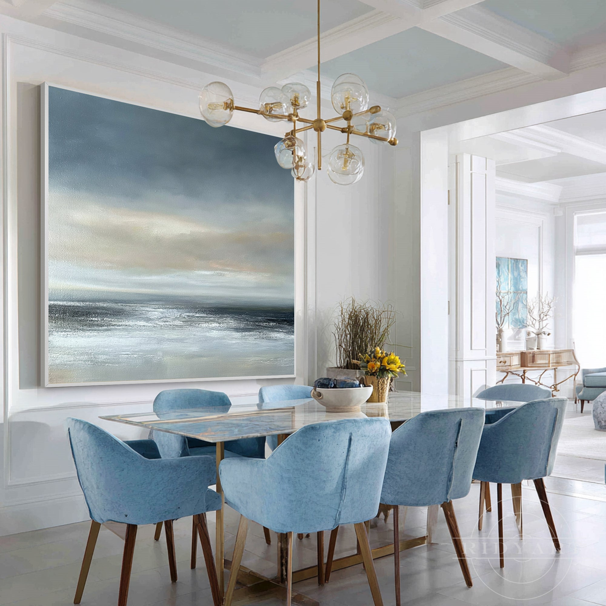 Square grey and blue seascape canvas painting displayed above a dining table surrounded by light blue velvet chairs.