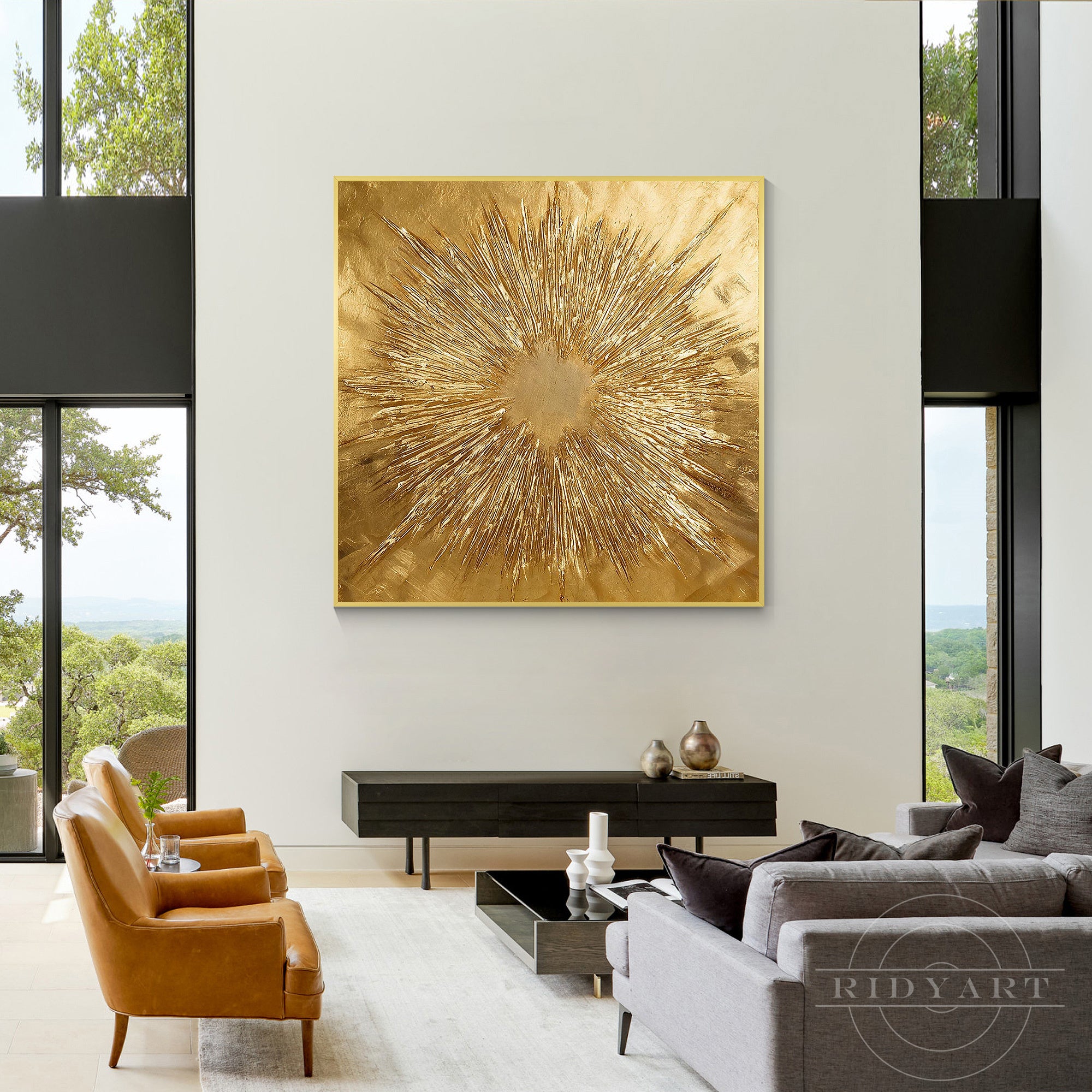 Oversized square gold sunburst artwork centered over a modern fireplace in a luxury living room with dark blue velvet sofas and ottomans.