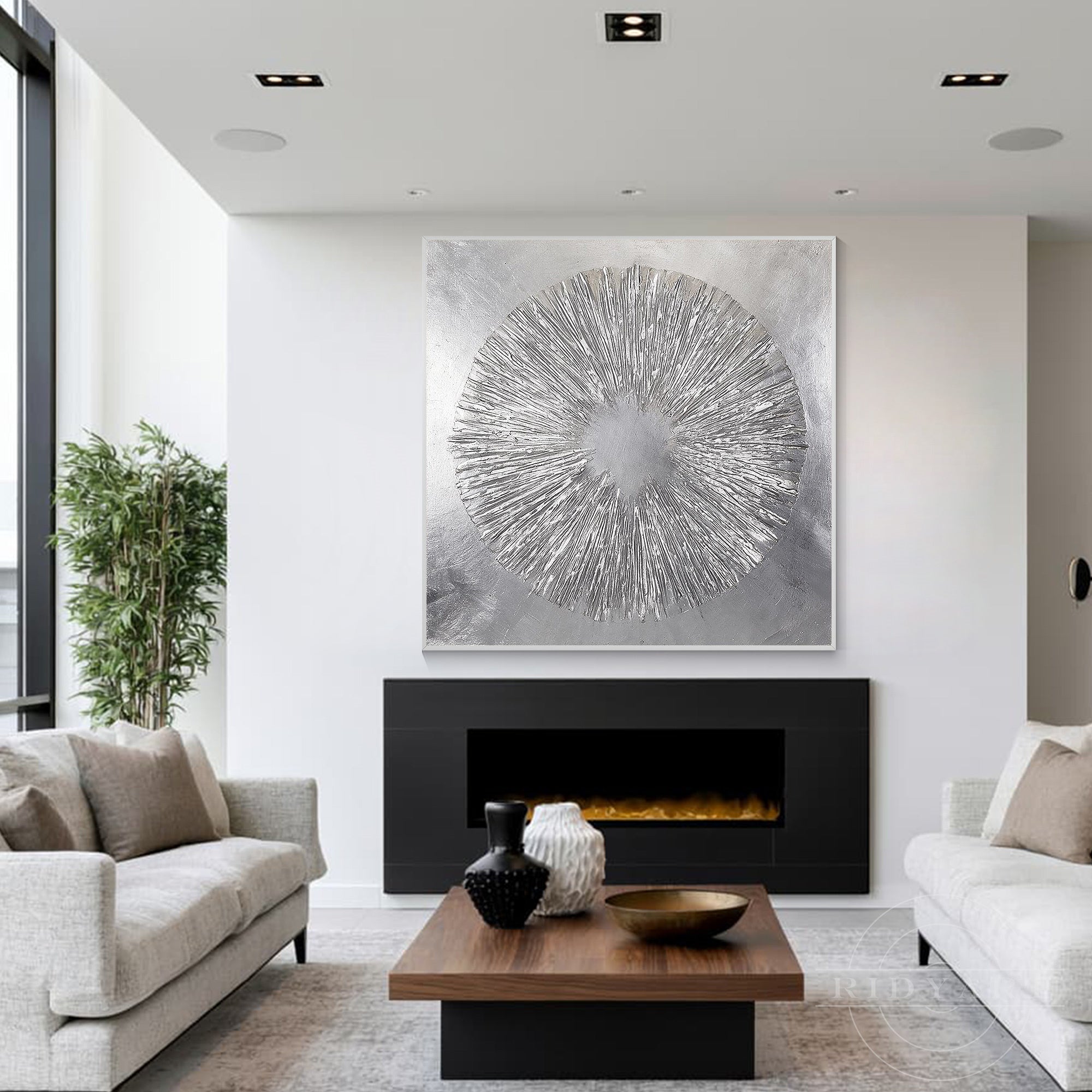 Textured silver starburst canvas art displayed over a sleek black modern fireplace between two cream sofas.