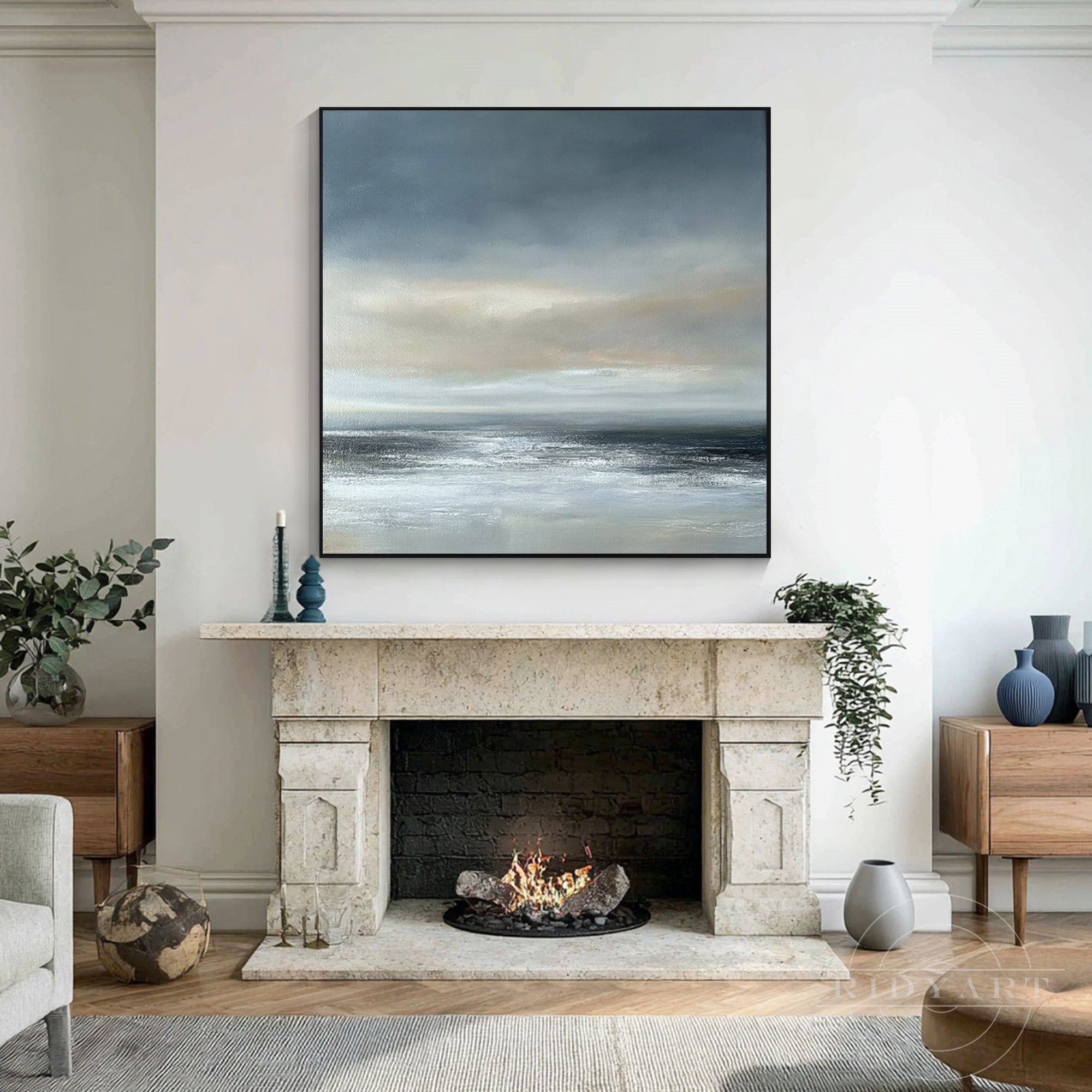 Moody blue and grey square abstract seascape canvas painting hanging directly above a classic marble fireplace mantle in a warm modern home.