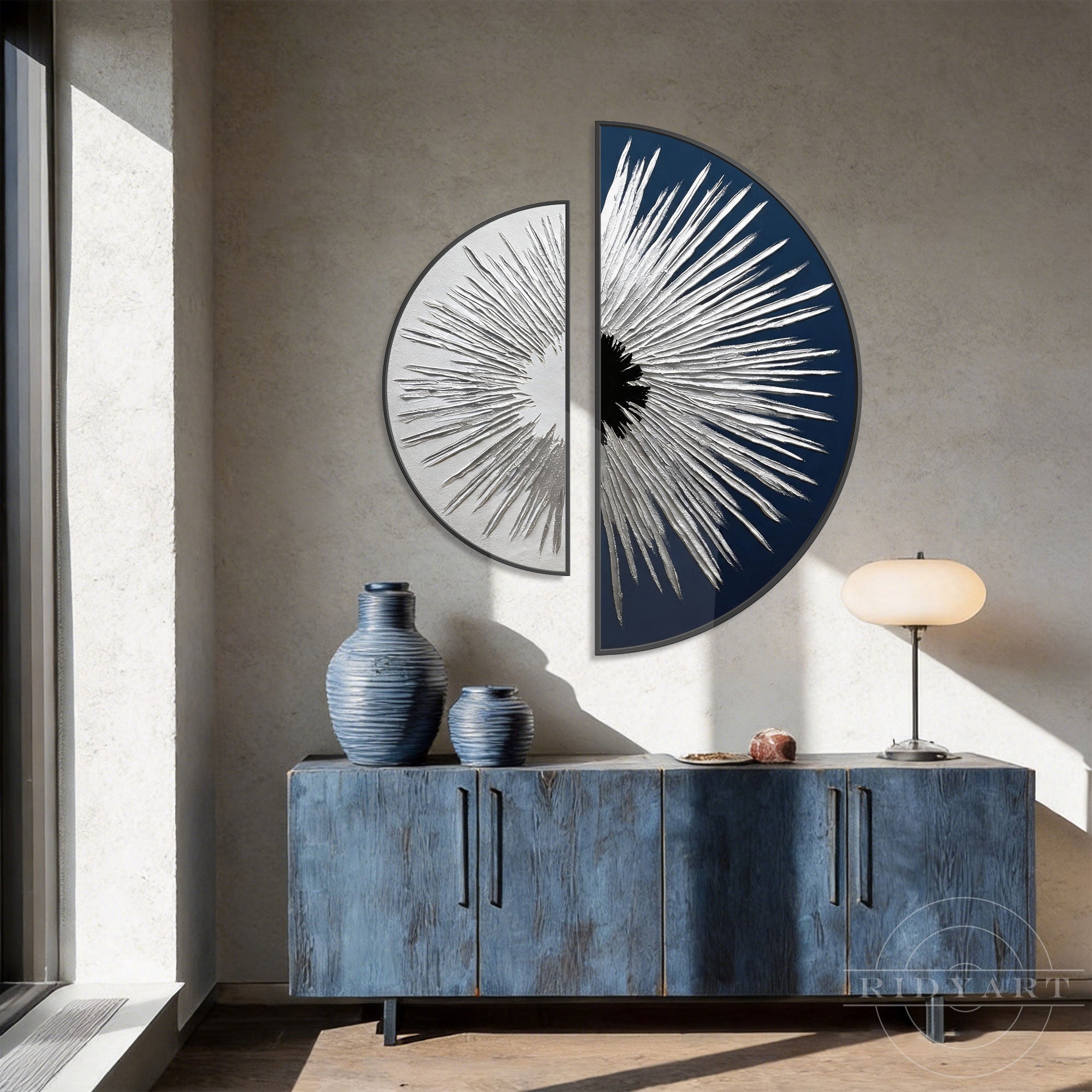 This modern 2-piece set of half round circle paintings showcases a dynamic textured silver sunburst design against contrasting white and navy blue backgrounds. The abstract wall art is elegantly displayed above a rustic blue wooden console cabinet, creating a sophisticated artistic focus in the room.